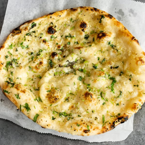 Close-up of Nanglo Restaurant's garlic naan, a flatbread topped with green herbs and charred spots.