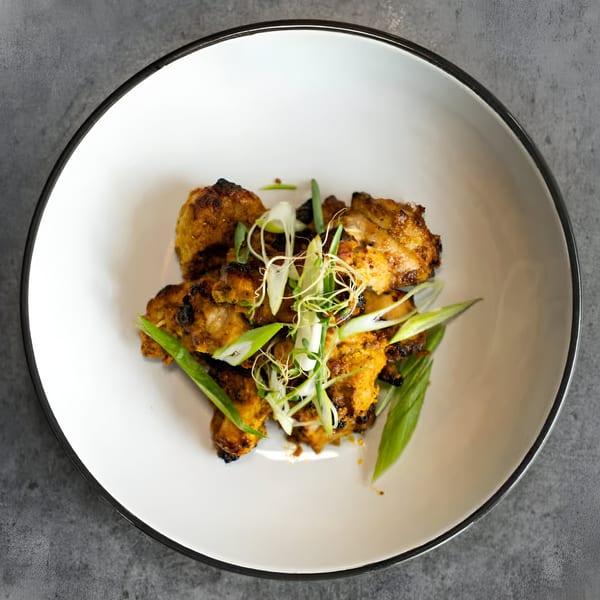 Nepalese chicken choila, garnished with fresh green onions and sprouts, in a white bowl.