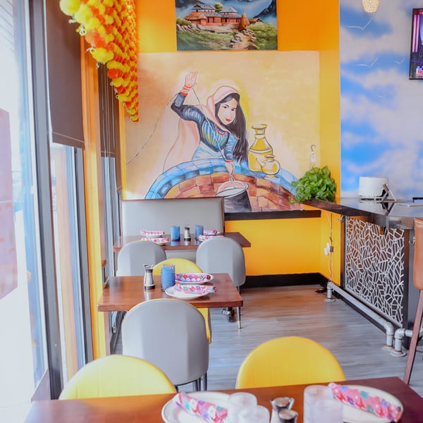 Nanglo Restaurant's dining area with colorful murals, set tables, and yellow and gray chairs.