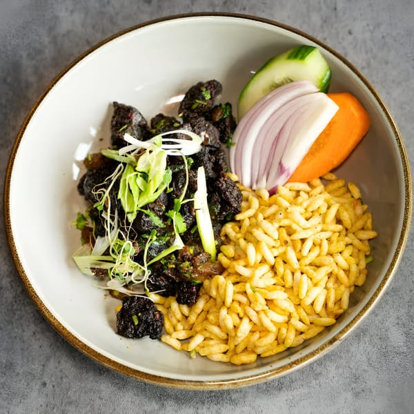 Nanglo's Nepalese dish with dark meat, puffed rice, sliced red onion, cucumber, and green garnish.