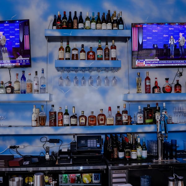 A well-stocked bar at Nanglo Restaurant, featuring various liquor bottles, wine glasses, and two TVs.