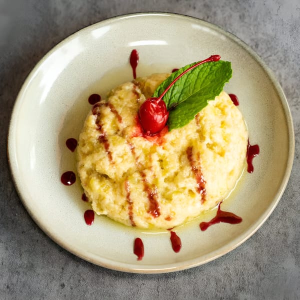 Creamy Nepalese dessert with red syrup, a cherry, and mint on a light plate.