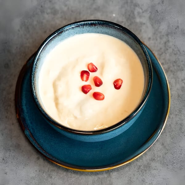 Creamy white dessert with red pomegranate seeds in a blue bowl on a matching plate.