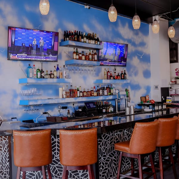 A well-stocked bar at Nanglo Restaurant and Bar, featuring brown leather stools and a cloud-painted wall.