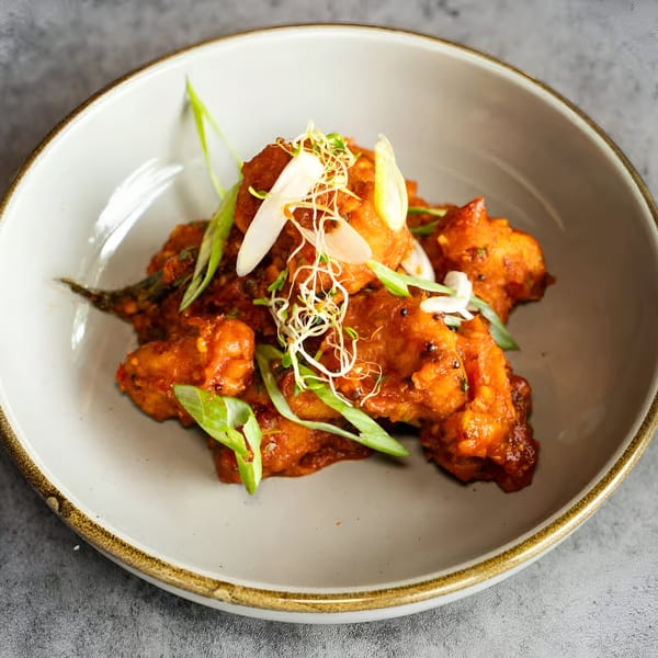 Nanglo Restaurant's Nepalese chili chicken, garnished with green onions and sprouts in a bowl.