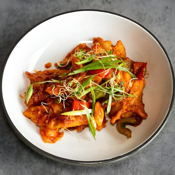 Nepalese chili chicken, garnished with spring onions and sprouts, in a white bowl.