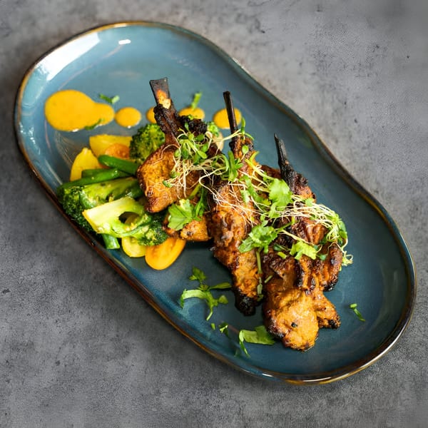 Nanglo Restaurant's Nepalese lamb chops with broccoli, yellow peppers, and a yellow sauce on a blue plate.